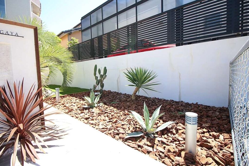 リゾート感のある洋風オシャレ外構。白い門柱とウッドチップを組み合わせた植栽で高級感の演出。